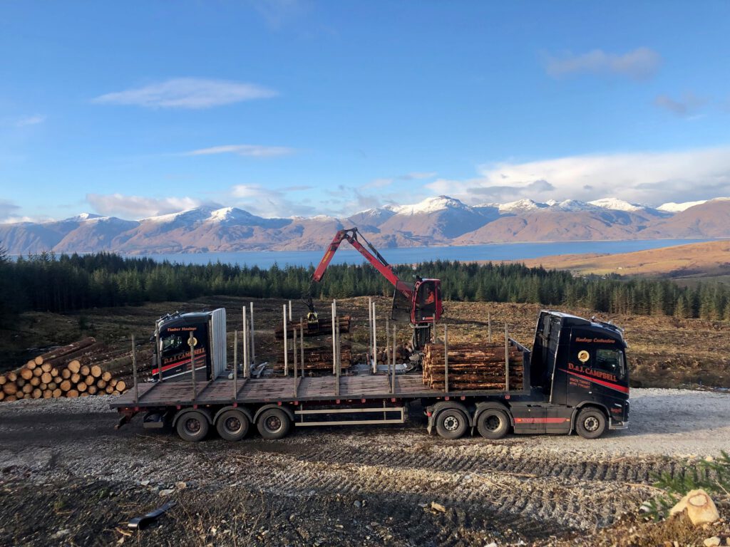 D&J Campbell Volvo timber lorry loading logs with Highland mountains behind